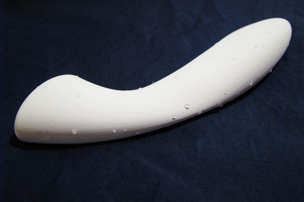 The LELO Ella, a white dildo with a flat tip, lying on a dark blue sheet. It is slightly wet.