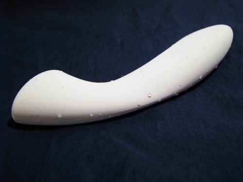 The LELO Ella, a white dildo with a flat tip, lying on a dark blue sheet. It is slightly wet.