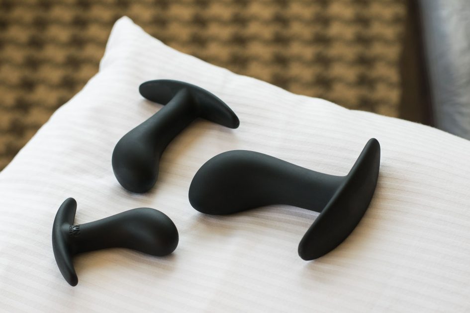 Three Fun Factory Booties, one of each size, on a white sheet, with patterned carpet in the background.