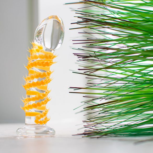 The Taffy Tickler Silicone Sweets glass dildo, covered in little orange spikes, standing upright near some pointy green fake grass.