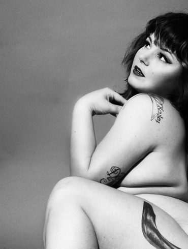 Courtney Trouble, nude, in a black and white shot showing off their high heel tattoo.