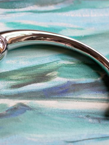 njoy Pure Wand stainless steel G-spot dildo on a painting of the ocean waves.