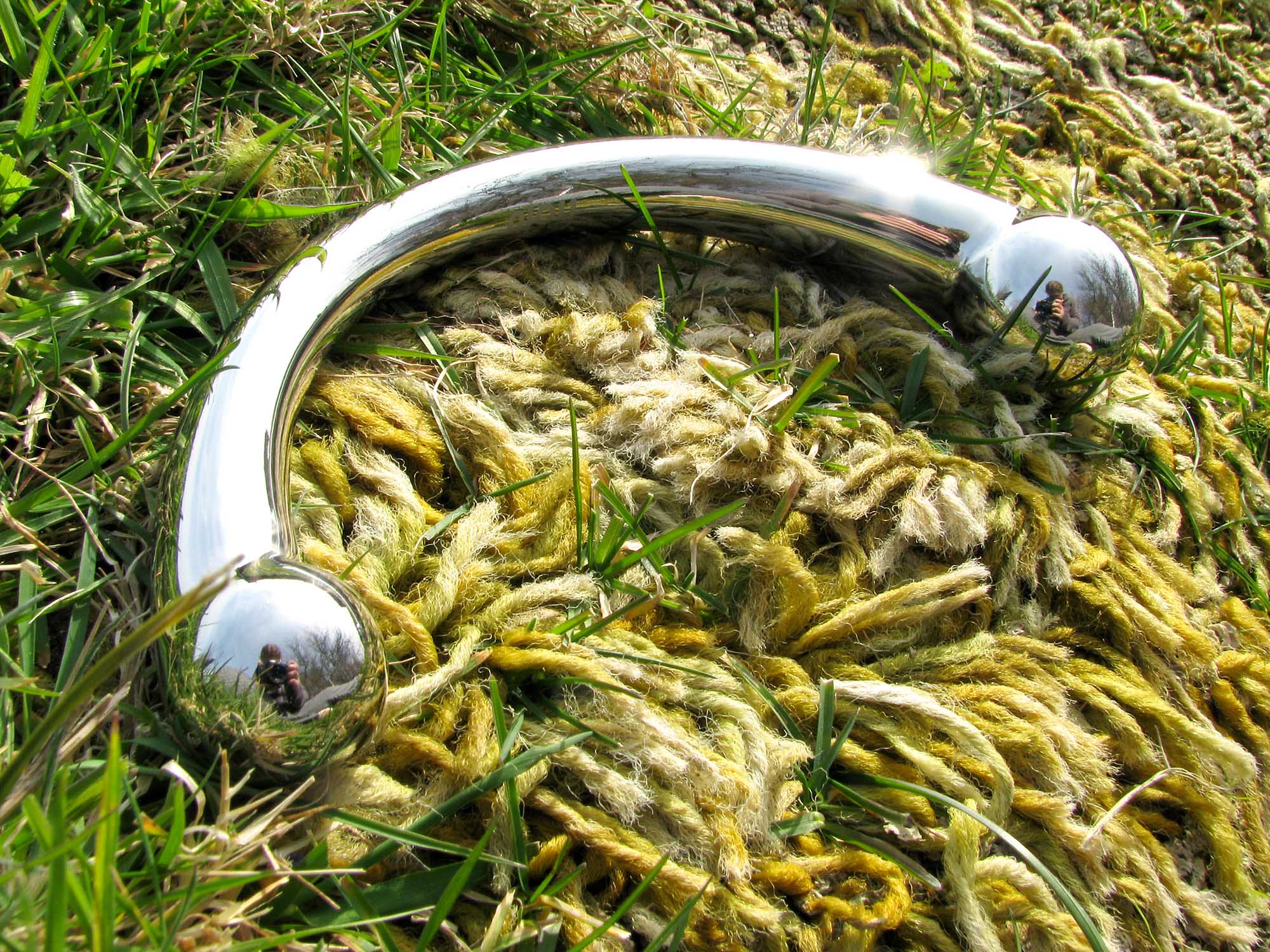 njoy Pure Wand stainless steel G-spot dildo on the ground, with golden shag carpet growing through the grass.