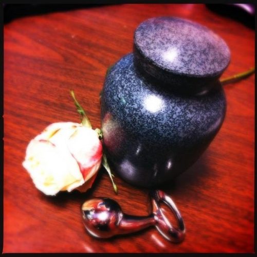 A fancy urn on a wooden table, with the Pure Plug and a rose next to it.