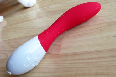LELO Mona 2 vibrator on a hardwood floor with some kitty feet in the background.