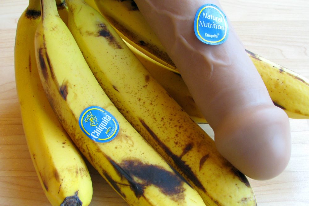 Vixen Creations Buck dildo with a bunch of bananas. Accordingly, the dildo has a Chiquita sticker on it that says NATURAL NUTRITION.