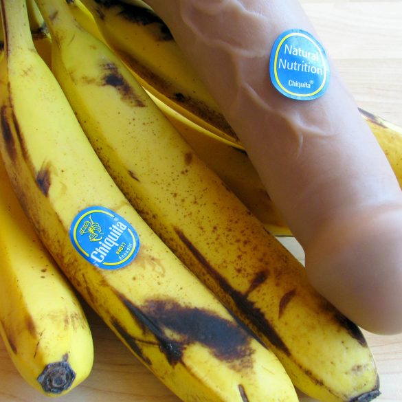 Vixen Creations Buck dildo with a bunch of bananas. Accordingly, the dildo has a Chiquita sticker on it that says NATURAL NUTRITION.
