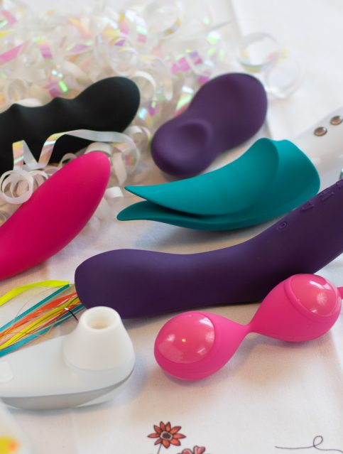 Colorful vibrators and kegel balls surrounded by iridescent curly ribbons.