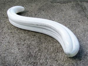 Fucking Sculptures G-Spoon large glass dildo on rough cement, with greenery in the background.