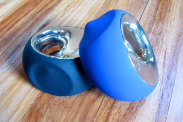 Black LELO Ora (original), blue LELO Ora 2 on a hardwood floor.