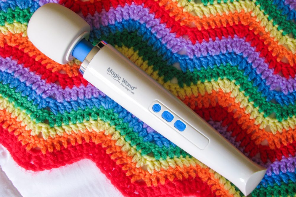 Hitachi Magic Wand Rechargeable vibrator on a zig-zag-patterned rainbow crocheted blanket.