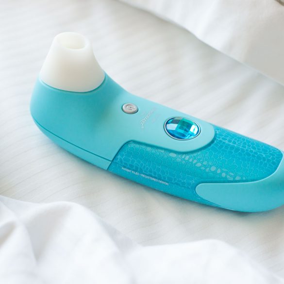 Womanizer air flow / pressure wave suction vibrator, with its ridiculous fake jewel, on a very white bed.
