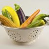 A literal colander full of silicone sex toys shaped like various vegetables and fruit: corn, carrot, eggplant, banana...