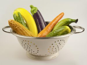 A literal colander full of silicone sex toys shaped like various vegetables and fruit: corn, carrot, eggplant, banana...