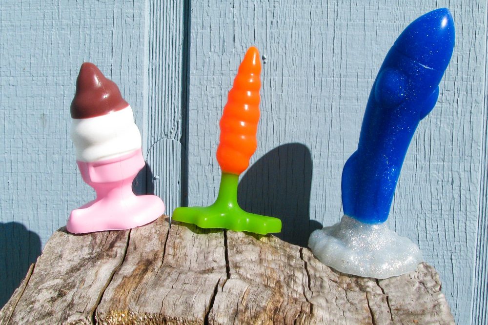 Hole Punch Toys Ass Cram Cone, Plugs Bunny, and Crotch Rocket standing on a wood pile in front of a pale blue house.