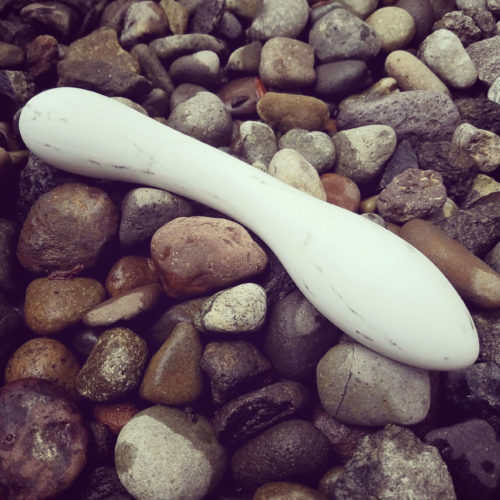 The Désirables Dalia, a white porcelain dildo lying on some stones.