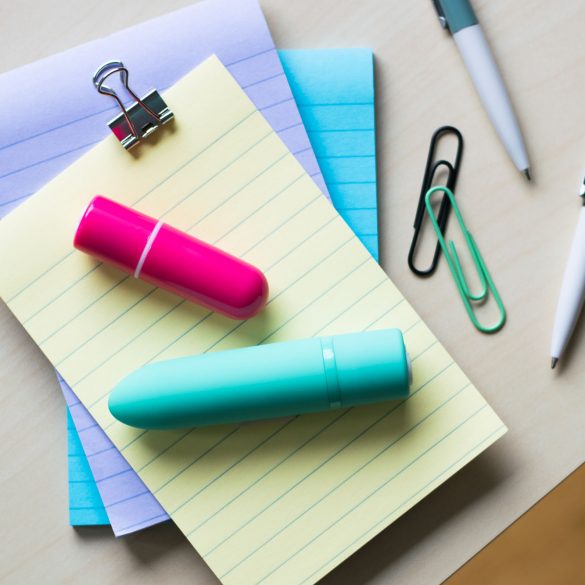 Screaming O Charged Vooom and Positive rechargeable bullet vibrators on top of a pile of colorful lined notepads.