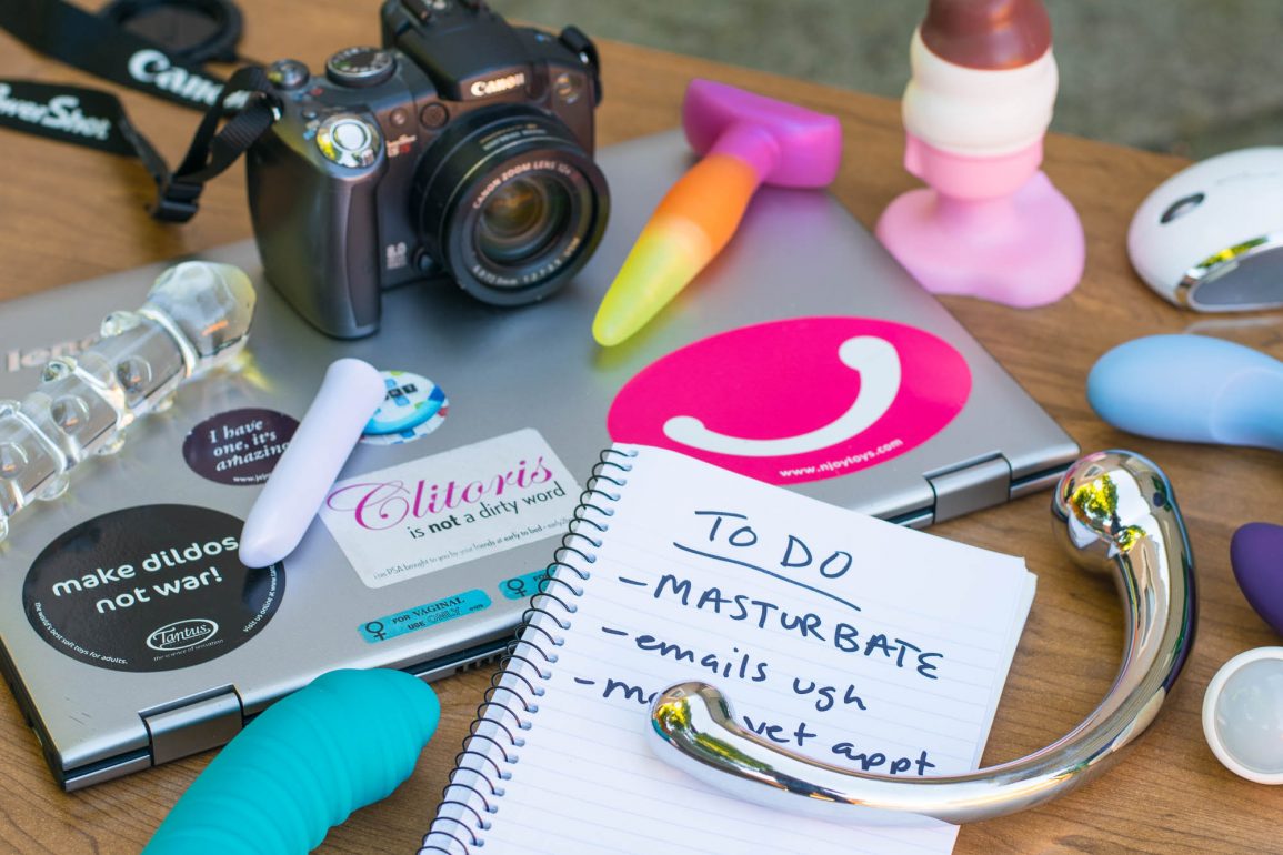Sex toy reviewer spread: camera, laptop, to-do list, and sex toys everywhere.