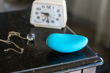 We-Vibe Wish rechargeable clitoral vibrator on a small table, next to a clock and necklace.
