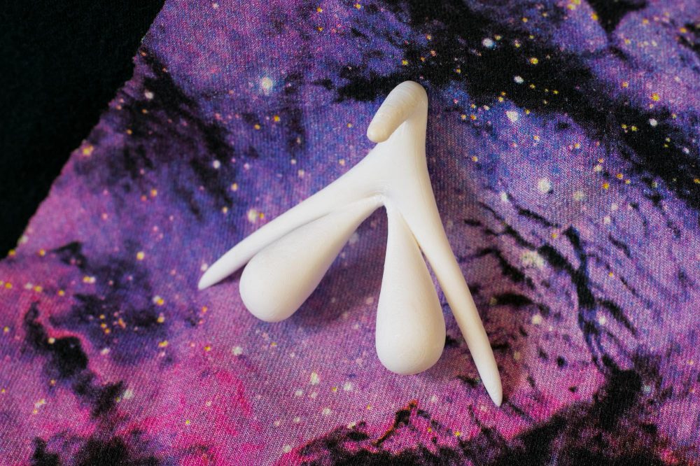 3D-printed clitoris organ, showing the entire external and internal structure, on a galaxy backdrop.