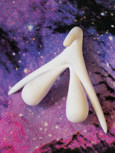 3D-printed clitoris organ, showing the entire external and internal structure, on a galaxy backdrop.