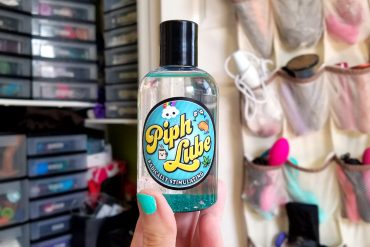 Piph Lube, with the glitter settled at the bottom, in front of my sex toy closet.