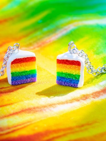Slice of rainbow pride cake necklaces on a tie-dye fabric