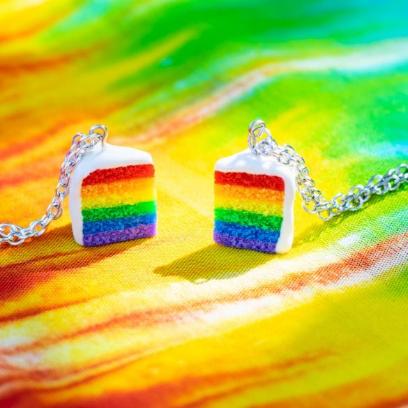 Slice of rainbow pride cake necklaces on a tie-dye fabric