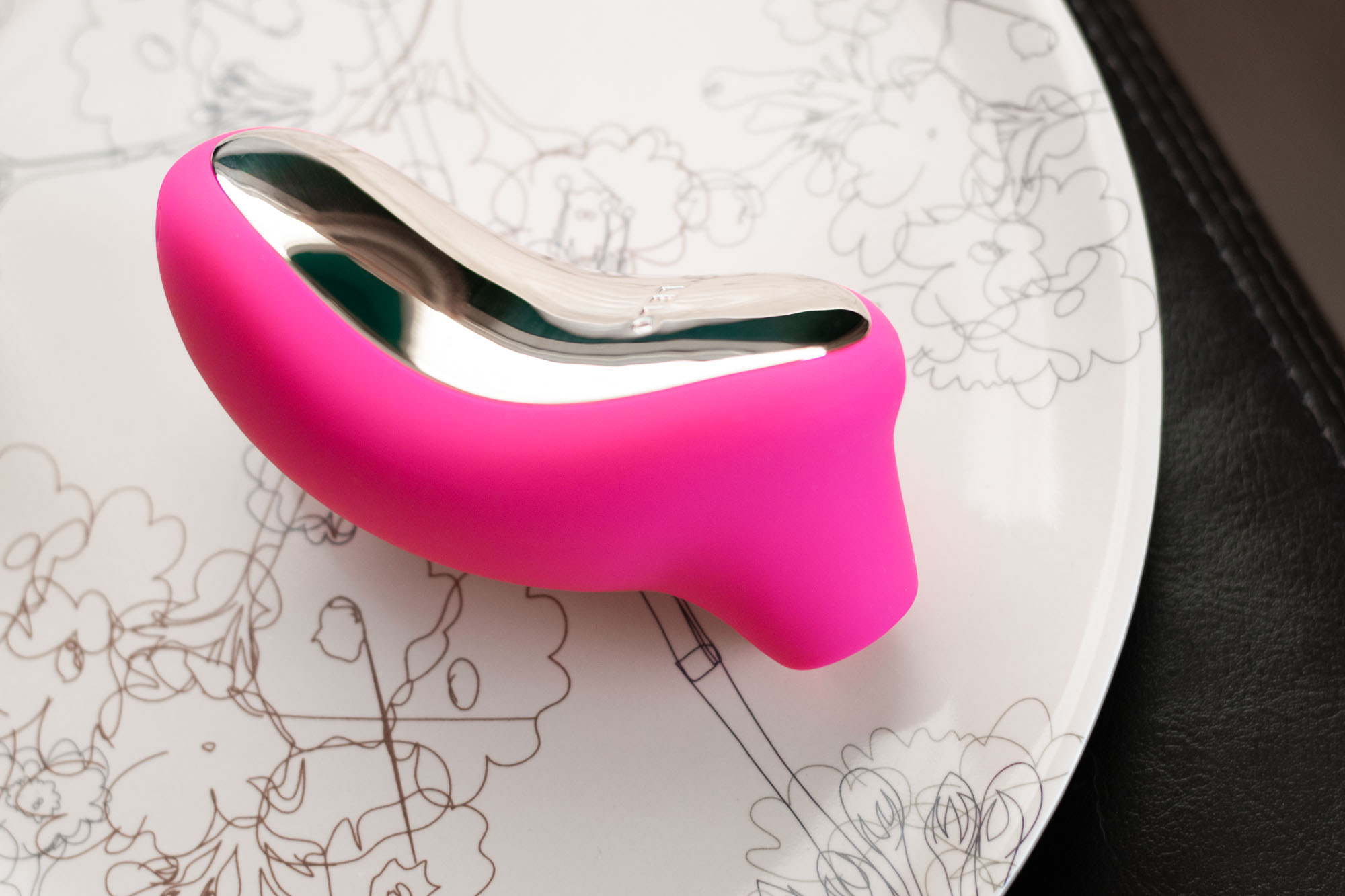 LELO Sona "sonic" air flow vibrator on a flower-patterned plate.