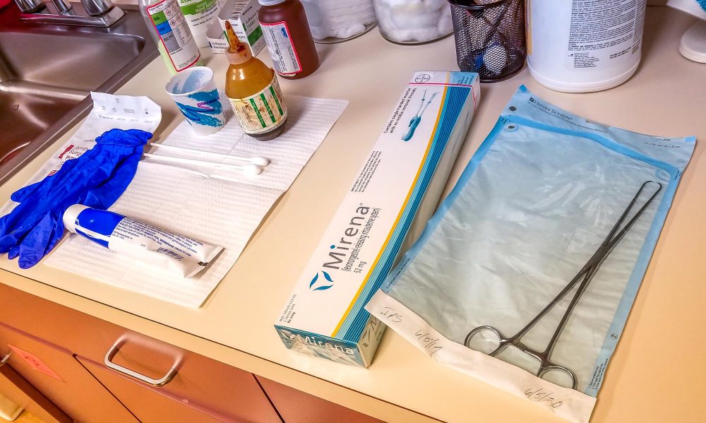 Supplies for Mirena IUD insertion laid out at the doctor's office, including forceps, lube, gloves, and the Mirena box.