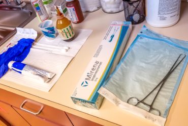 Supplies for Mirena IUD insertion laid out at the doctor's office, including forceps, lube, gloves, and the Mirena box.