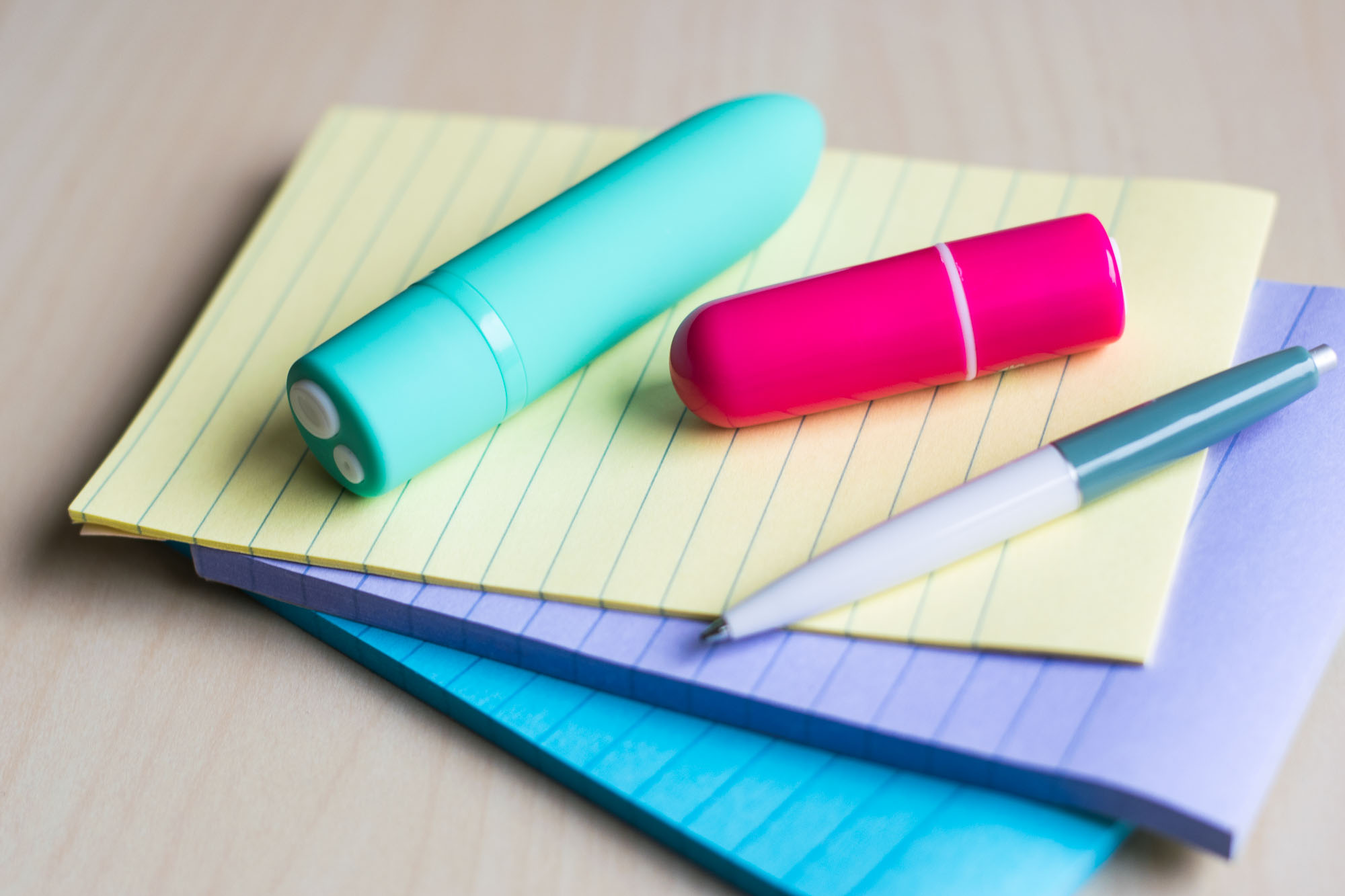 Screaming O Charged Positive and Vooom rechargeable bullet vibrators on top of a pile of colorful lined notepads.