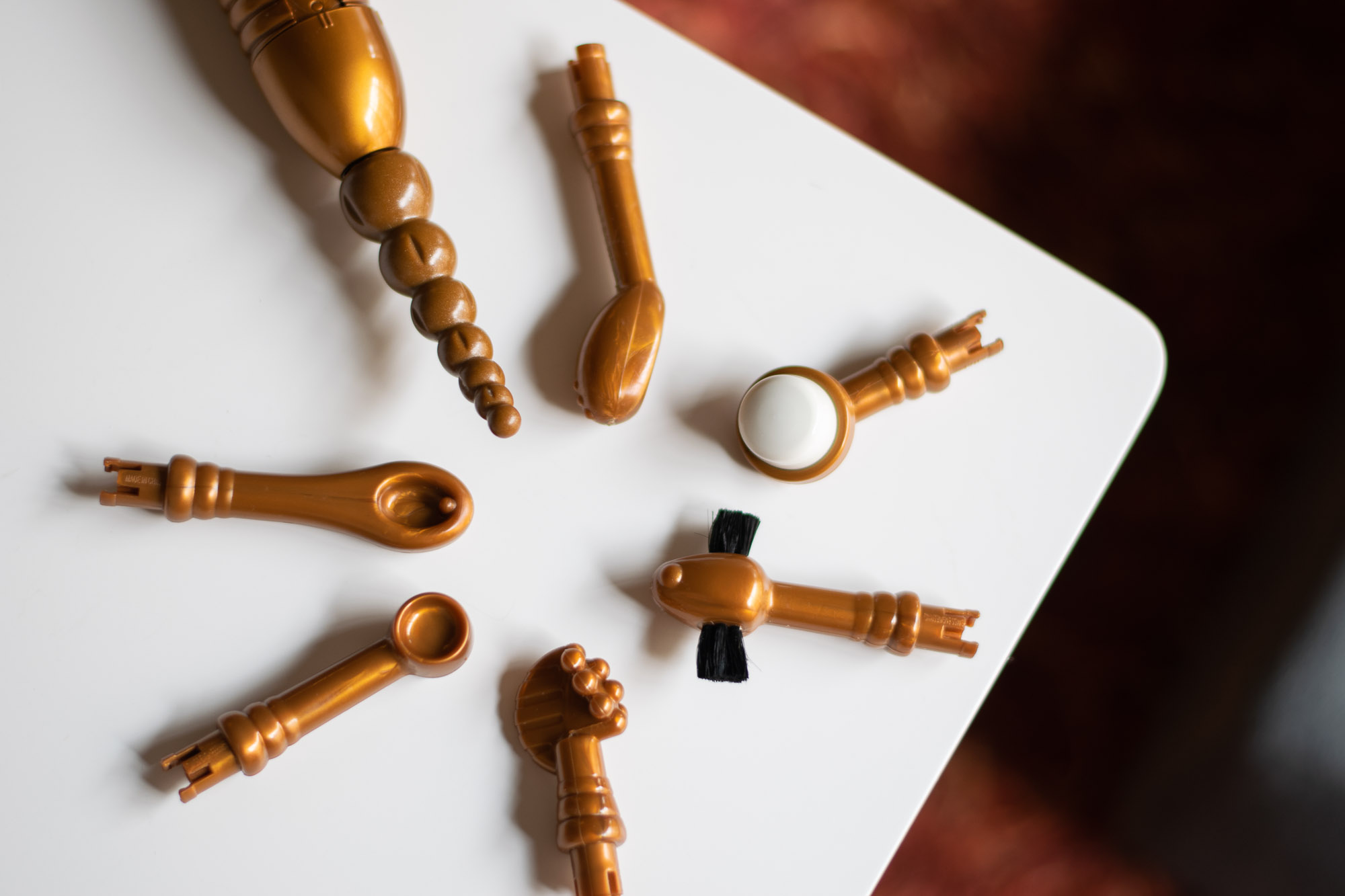 Eroscillator attachments in a circle on a white table: Seven Pearls of the Orient, G-Point, Ultra-Soft Finger Tip, French Legionnaire's Moustache, Grapes and Cockscomb, Ball and Cup, and Golden Spoon.