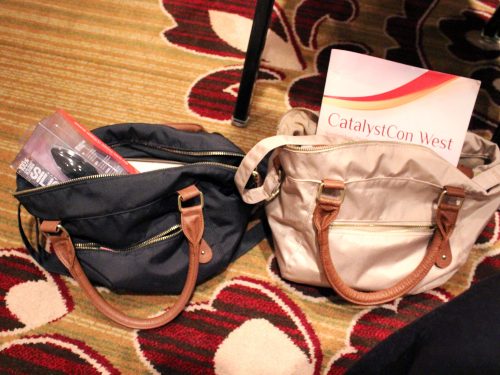 Similar bags, terrible carpet. Two purses next to each other, stuffed with conference paraphernalia.