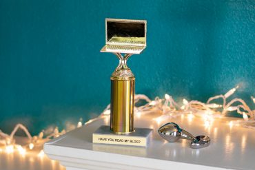 A trophy with a laptop on top, which reads, "HAVE YOU READ MY BLOG?" Next to it, a stainless steel butt plug.