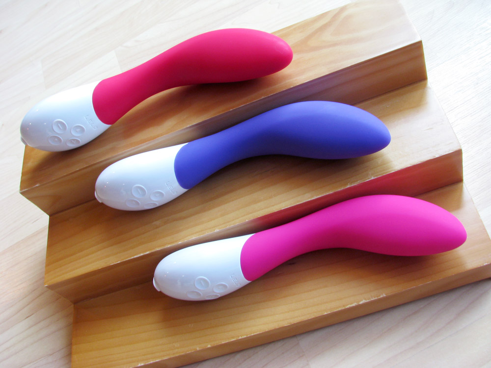 LELO Mona 2 in all three colors (red, purple, pink AKA cerise) on a graduated wooden shelf.