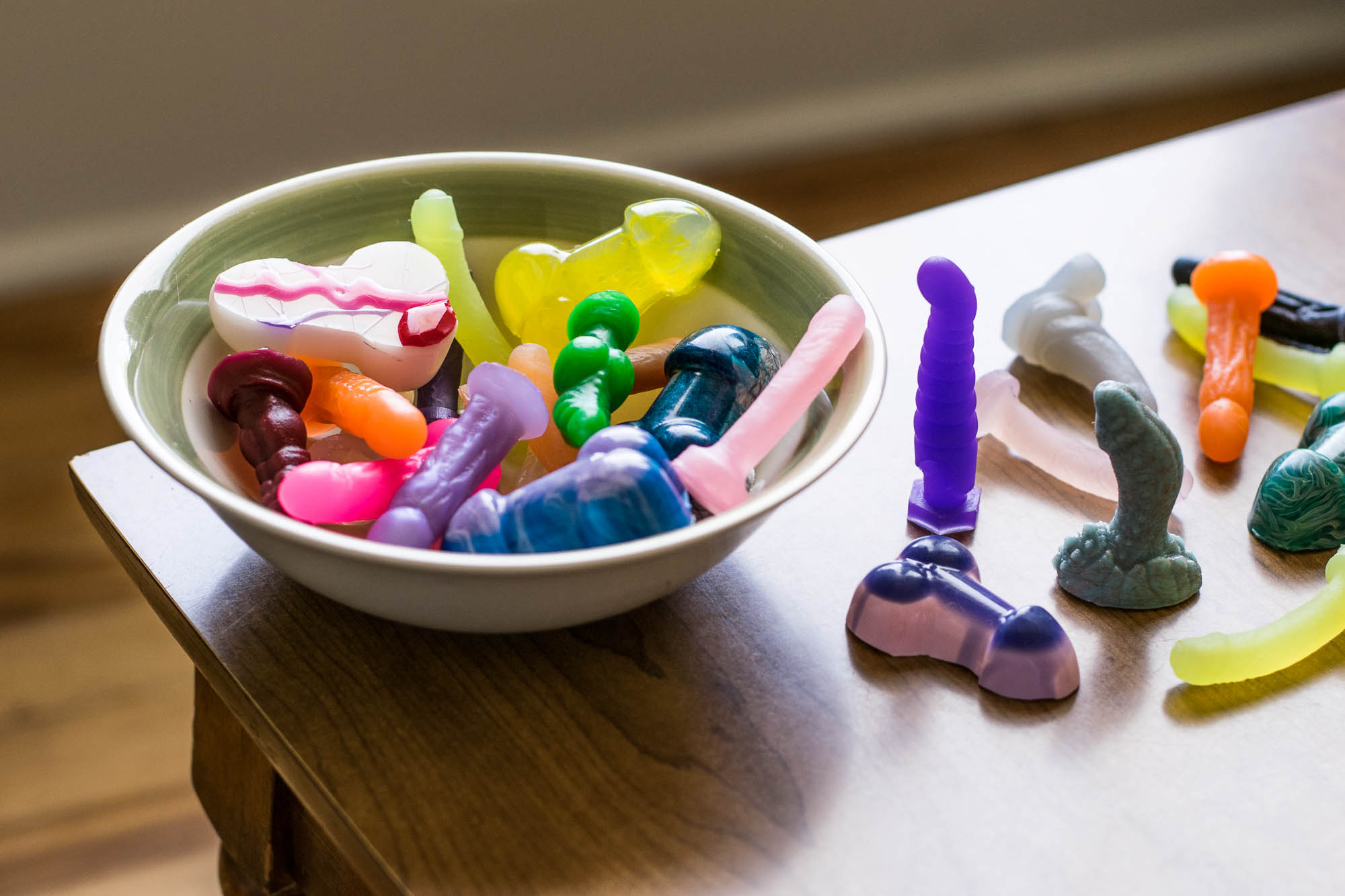 Tiny dildos from Vamp, Tantus, Bad Dragon and Fun Factory in a bowl and on a table.