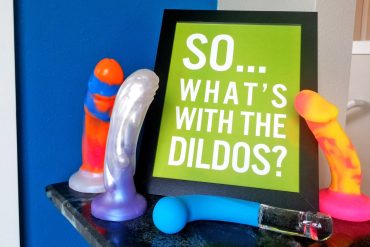 A sign reading "SO... WHAT'S WITH THE DILDOS?" surrounded by dildos.