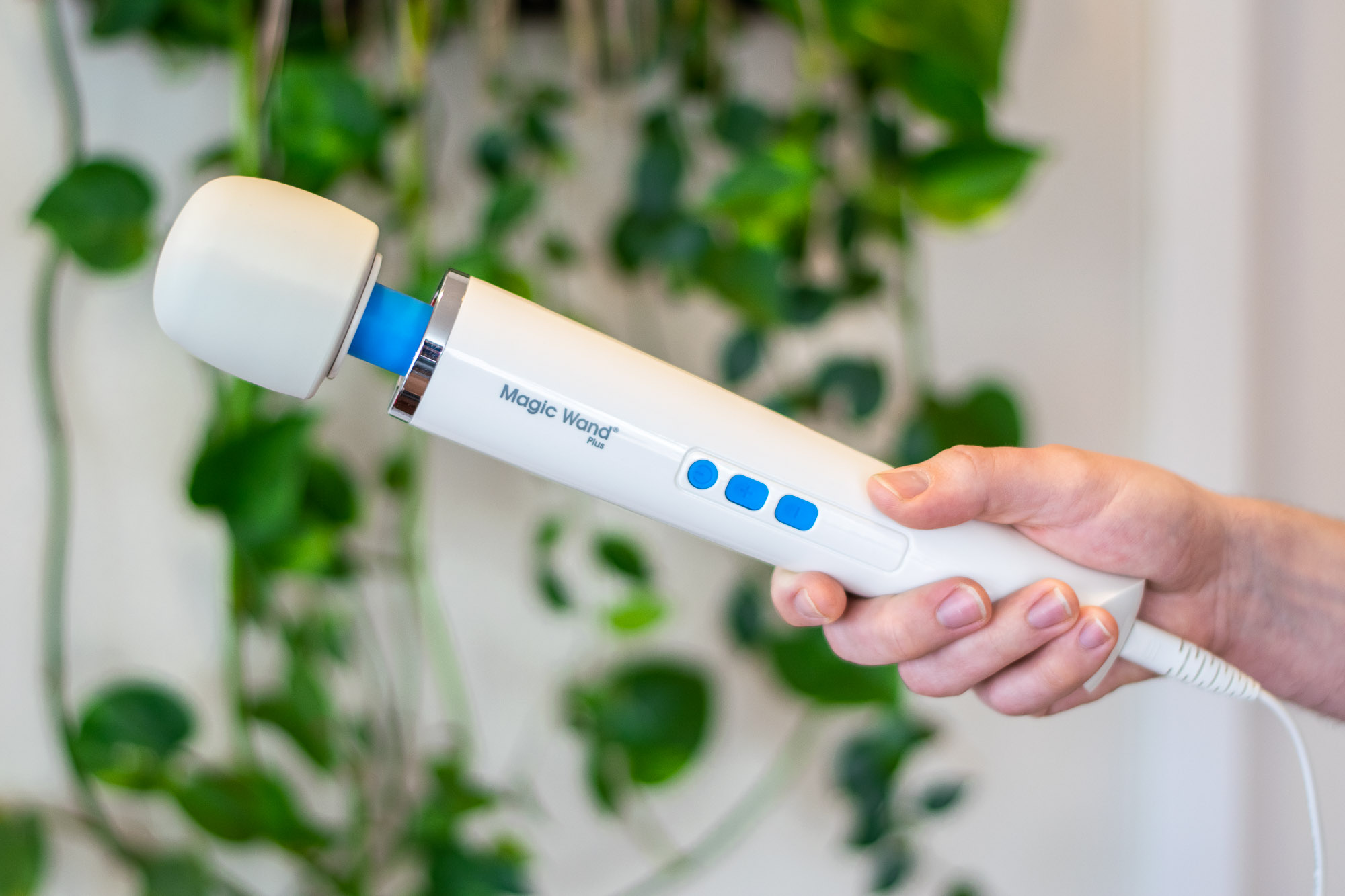 A person holding the Vibratex Magic Wand Plus corded vibrator in front of a green plant.