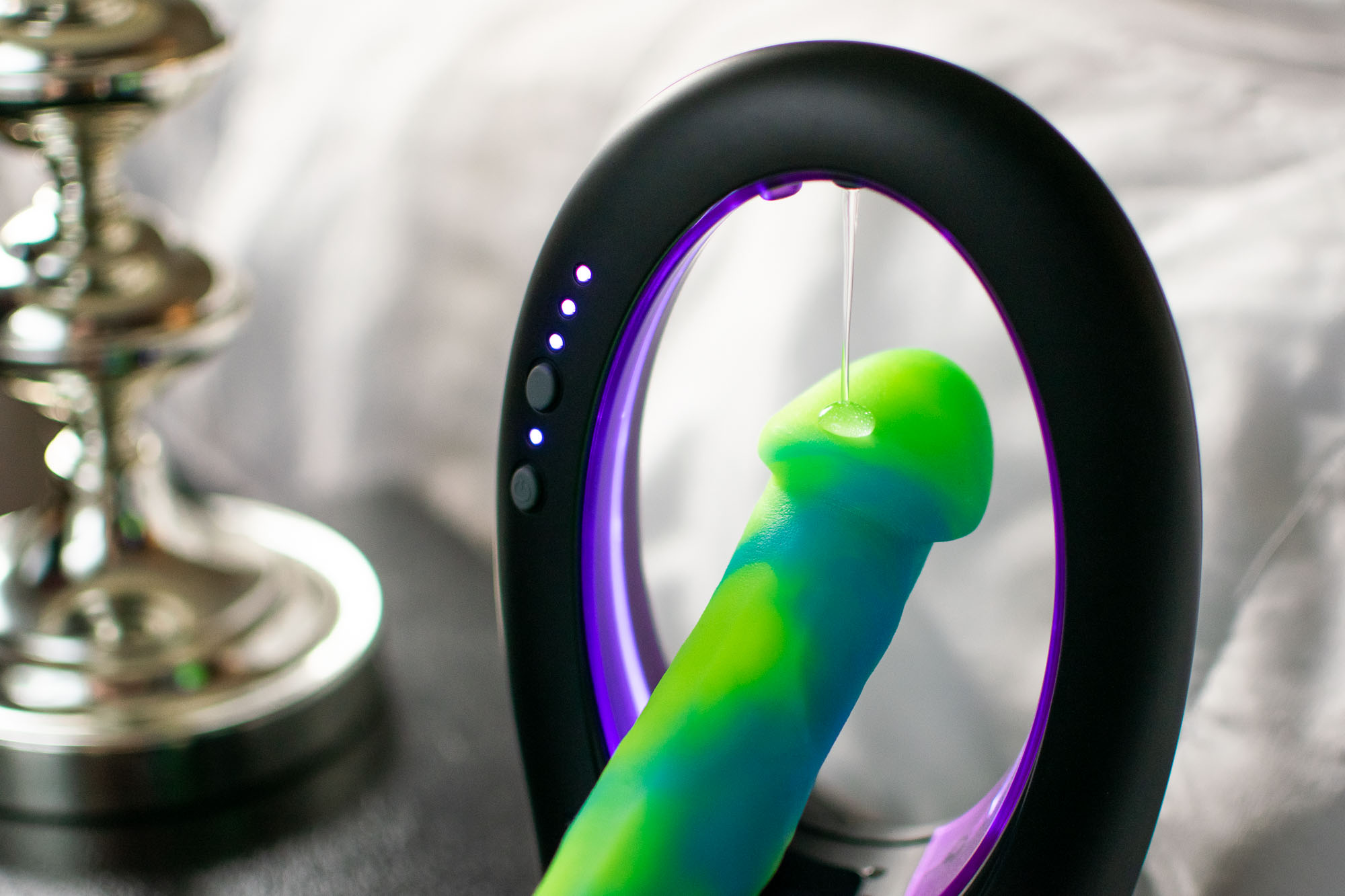 Warm Touch automatic warming lube dispenser dispensing a dollop of lube on a green and blue swirled dildo.
