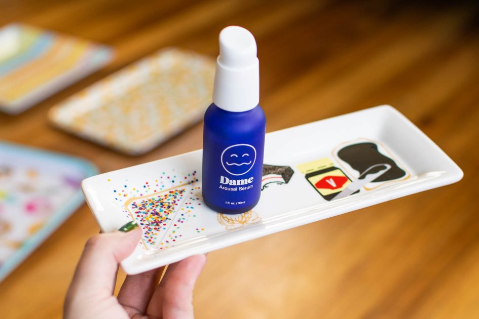 Blue glass bottle of Dame Arousal Serum on top of a small plate with Australian foods printed on it.