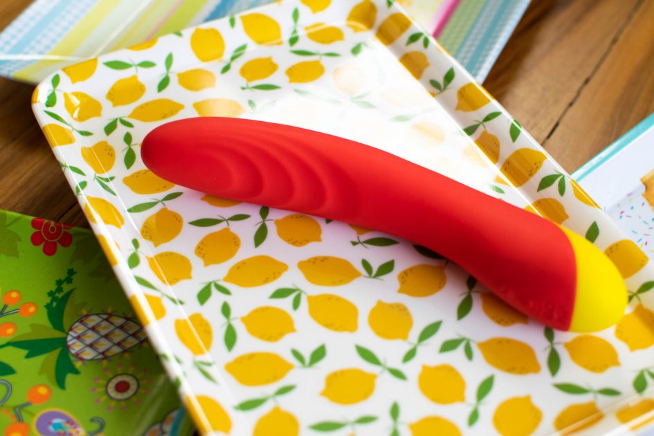 (We-Vibe/WOW Tech) Romp Hype rechargeable vibrator lying on a platter patterned with lemons.