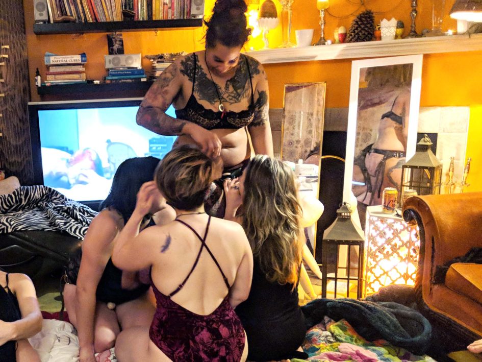 Three people on their knees, giving a simultaneous blowjob to a person wearing a strap-on.