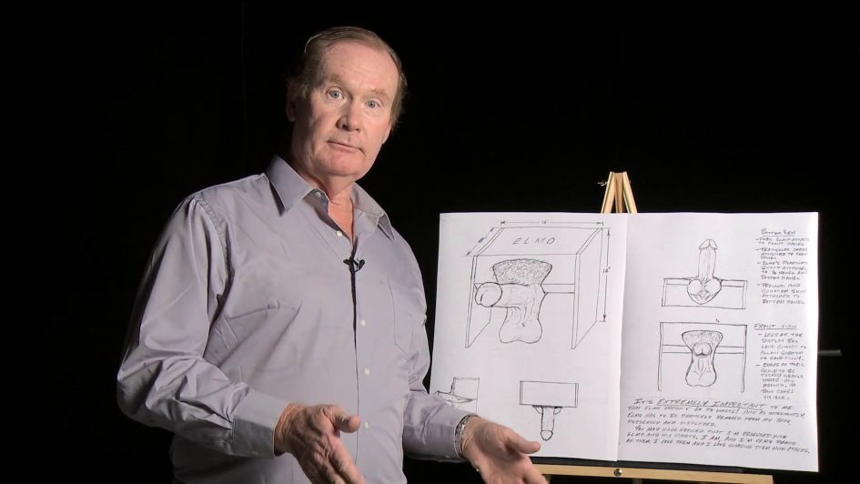 Tom in front of an easel showing all his plans for a box to display his severed penis.